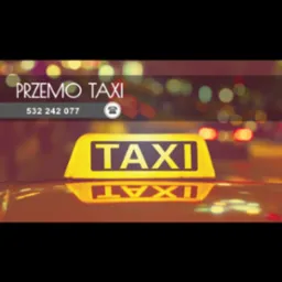 Żółty szyld TAXI z nazwą firmy i numerem telefonu na tle nocnego miasta. Widoczne odbicie szyldu na dachu samochodu.