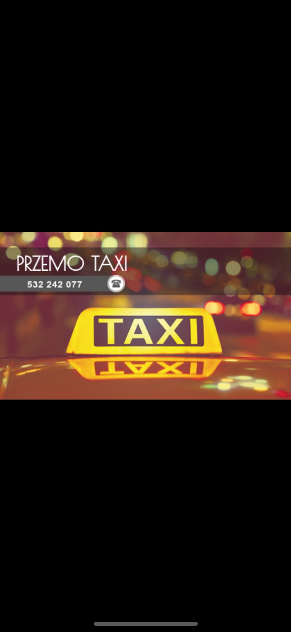 Żółty szyld TAXI z nazwą firmy i numerem telefonu na tle nocnego miasta. Widoczne odbicie szyldu na dachu samochodu.