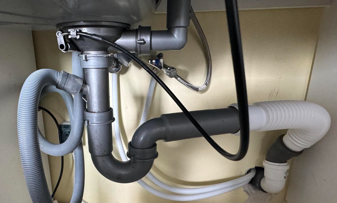 Szczegółowe ujęcie instalacji odpływowej pod zlewem, widoczne rury PCV i elastyczne węże w kuchni w Lublinie. Element wykończenia wnętrz.
