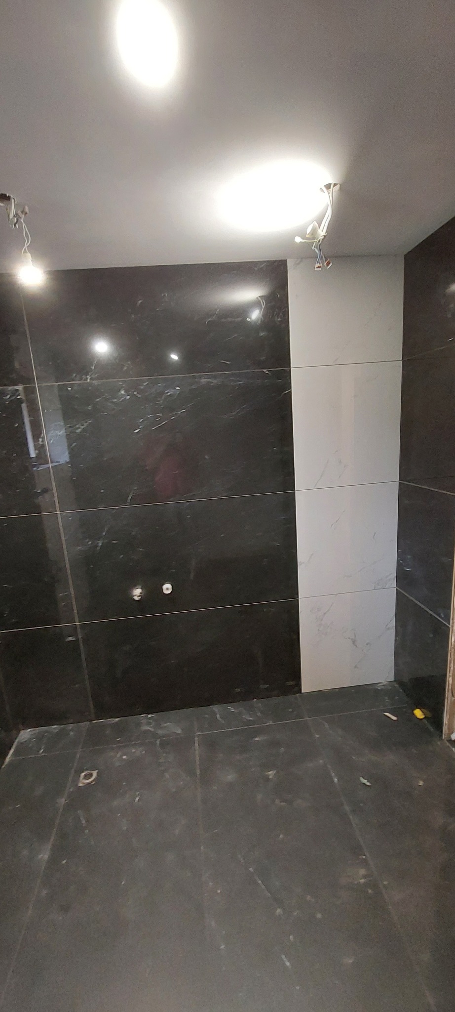 Wykończona łazienka z czarno-białymi płytkami imitującymi marmur na ścianach i podłodze. Widoczne punkty elektryczne i fragment instalacji oświetleniowej.