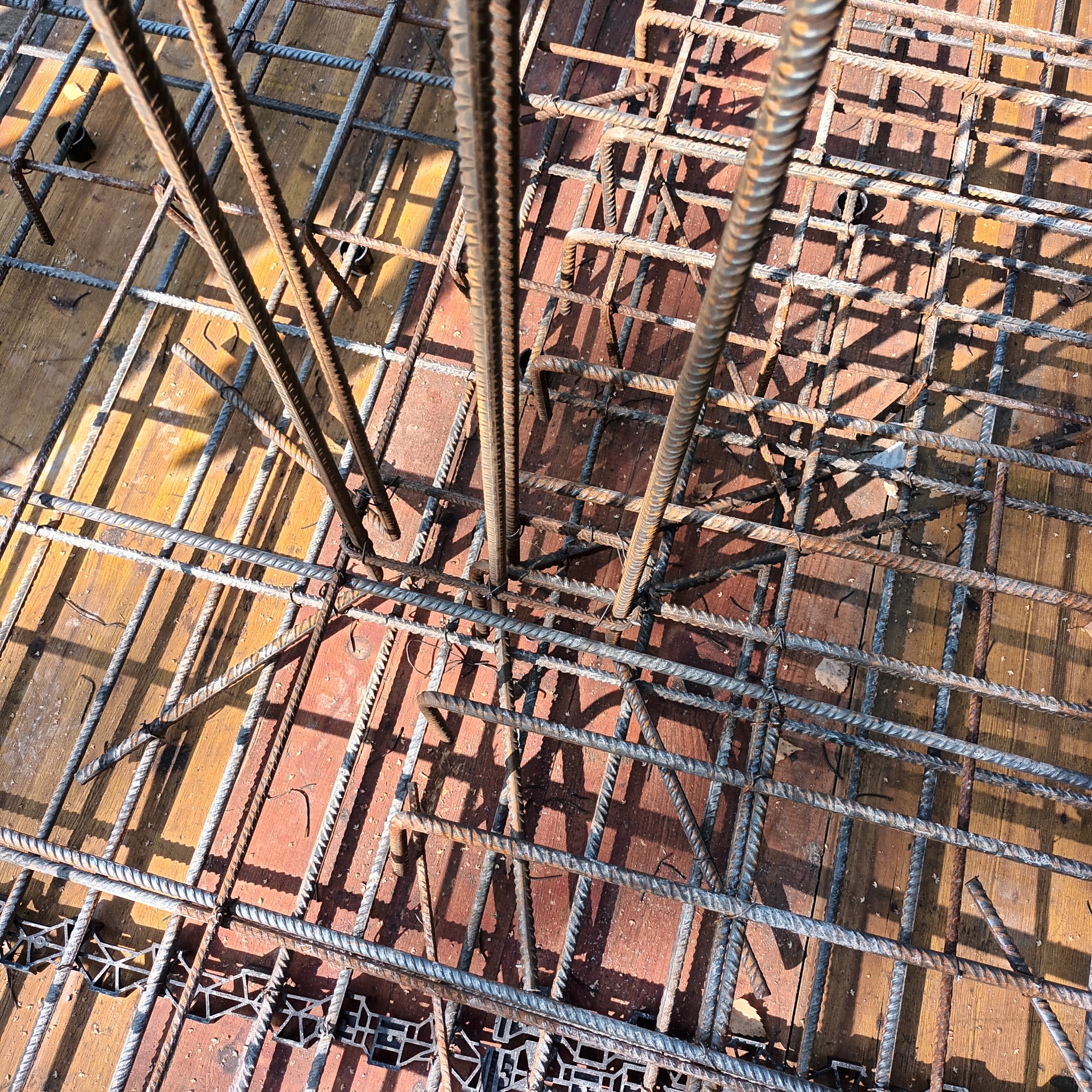 Zbrojenie fundamentu domu jednorodzinnego, widok z góry. Stalowe pręty tworzą siatkę na deskowaniu. Widoczne elementy dystansowe z tworzywa.