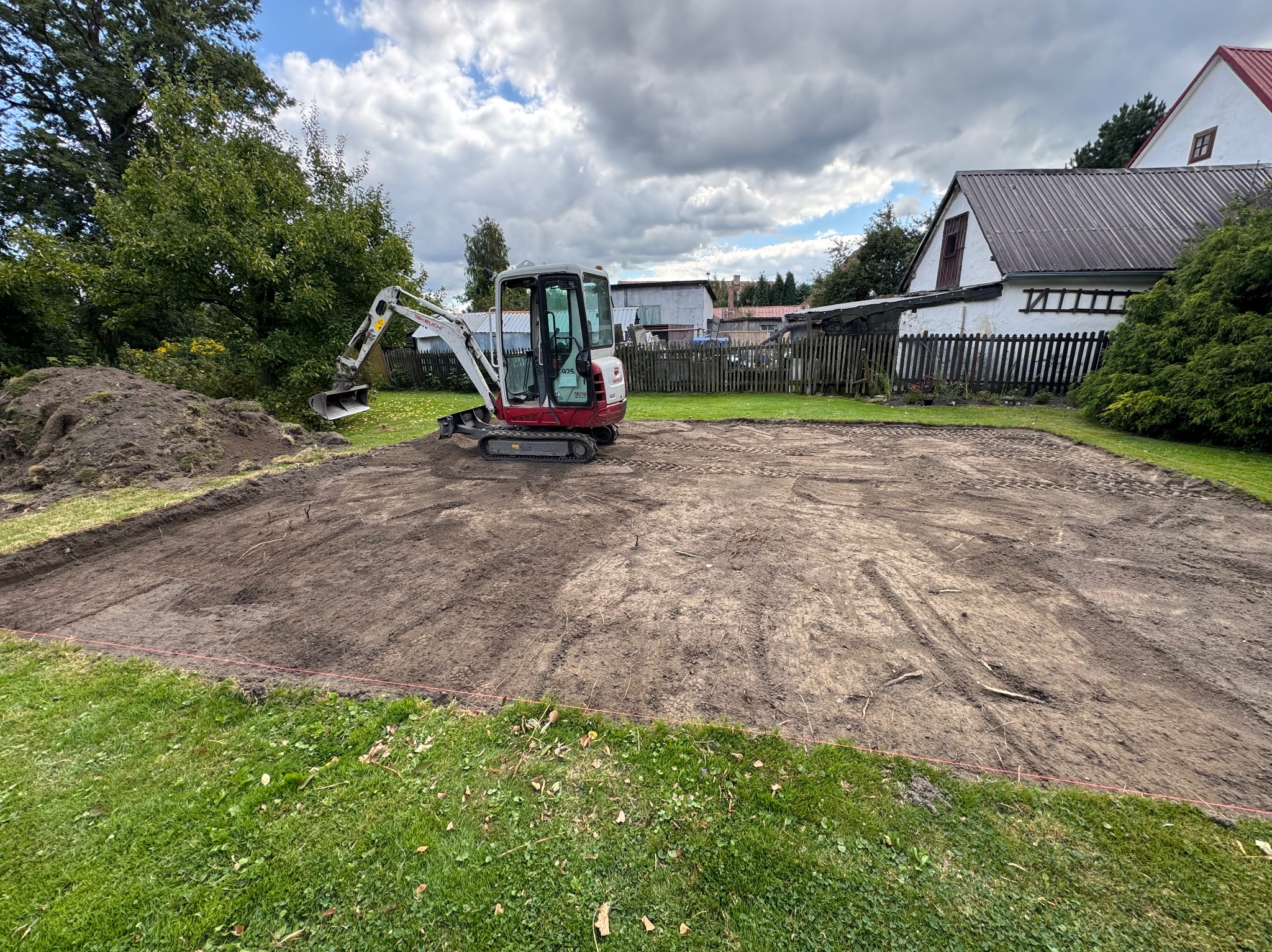Mini koparka na działce po niwelacji terenu, przygotowanej pod budowę. Widoczne ślady opon i wyznaczona granica działki czerwoną linką.