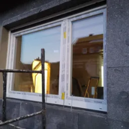 Montaż okna Salamander w ocieplonym budynku, widoczne rusztowanie i szara elewacja z izolacją.