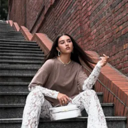 Modelka siedzi na schodach z torebką JWPEI, prezentując nową kolekcję. Ceglana ściana w tle, naturalne światło.