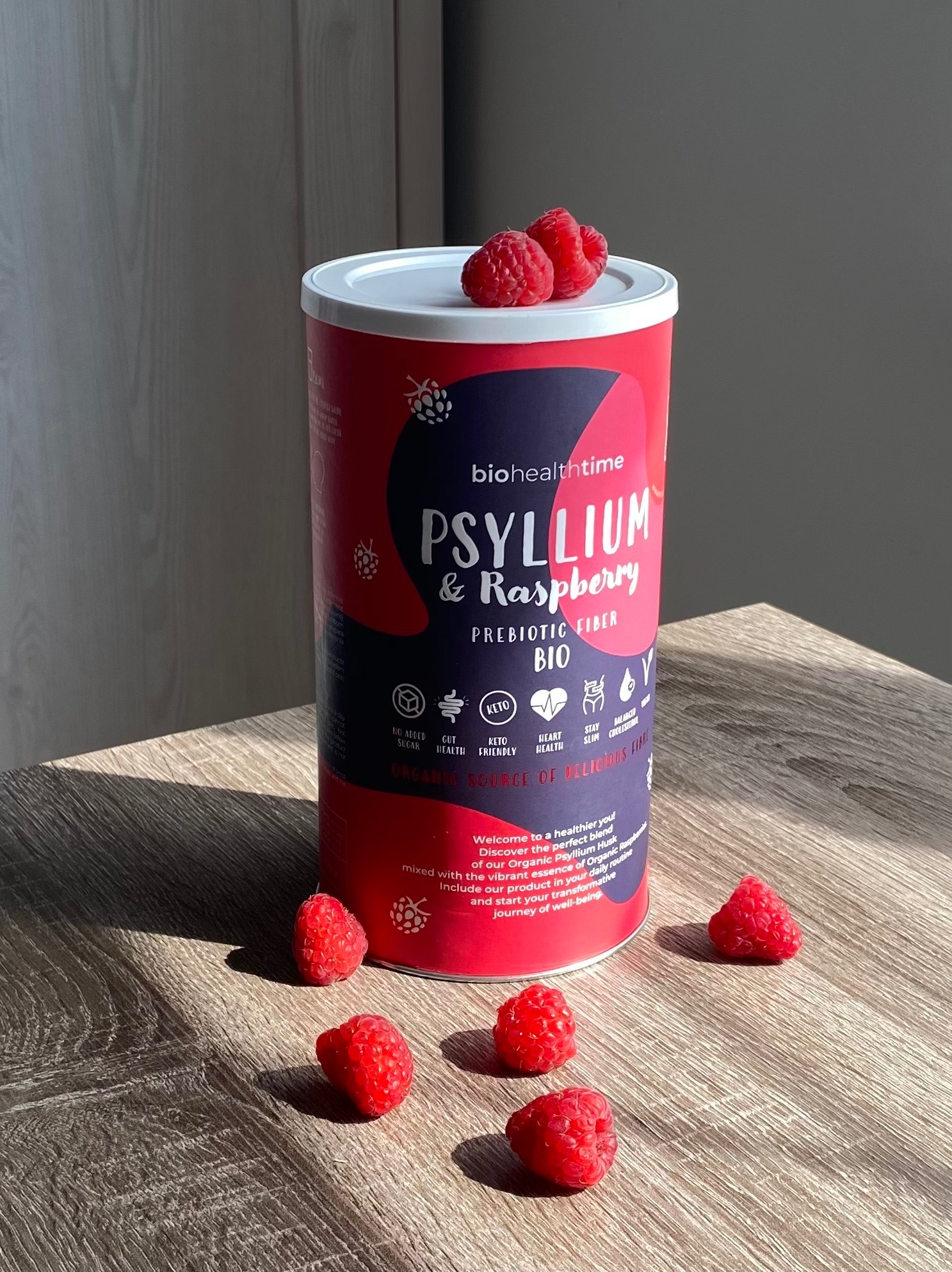 Puszka BioHealthTime Psyllium & Raspberry z malinami na drewnianym stole w naturalnym świetle. Fotografia produktowa prezentująca błonnik i jego właściwości.
