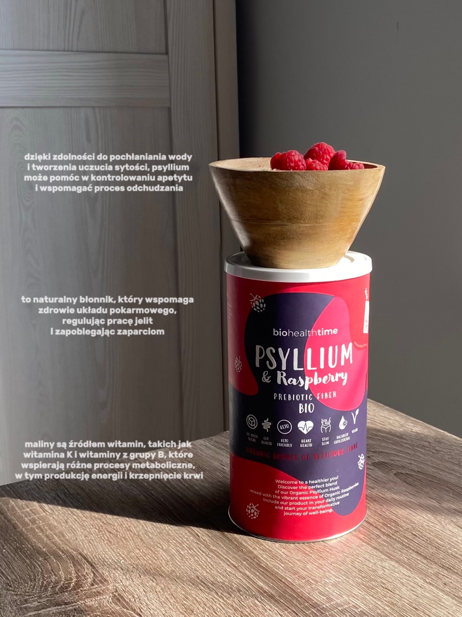 Zdjęcie produktu BioHealthTime: błonnik Psyllium & Raspberry BIO w puszce, z malinami w drewnianej miseczce na blacie. Naturalne światło, tekst informacyjny w tle.