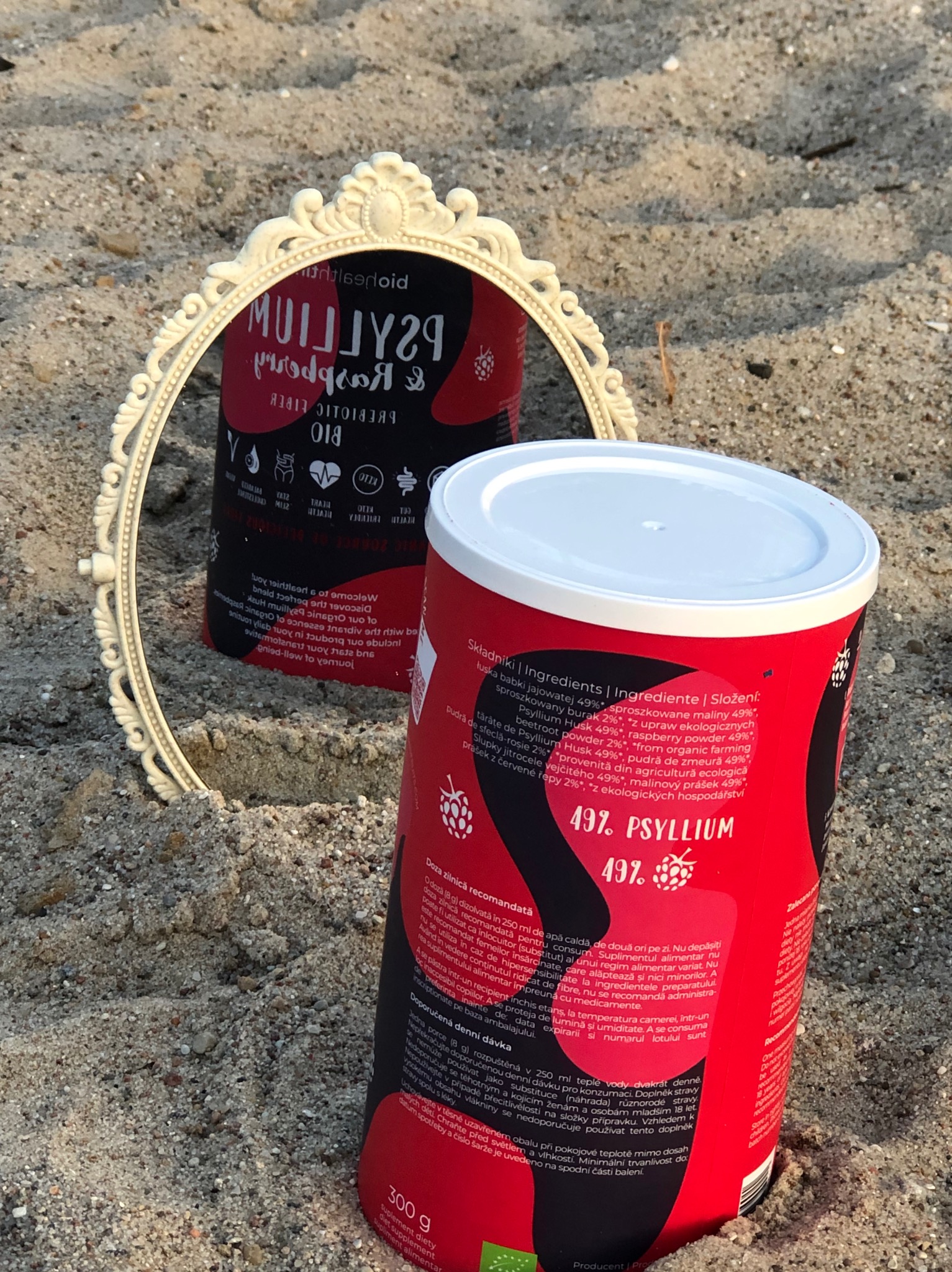 Produkt BioHealthTime (błonnik) w aranżacji: puszka na piasku, odbicie w ozdobnym lustrze. Fotografia produktowa podkreślająca naturalne właściwości.