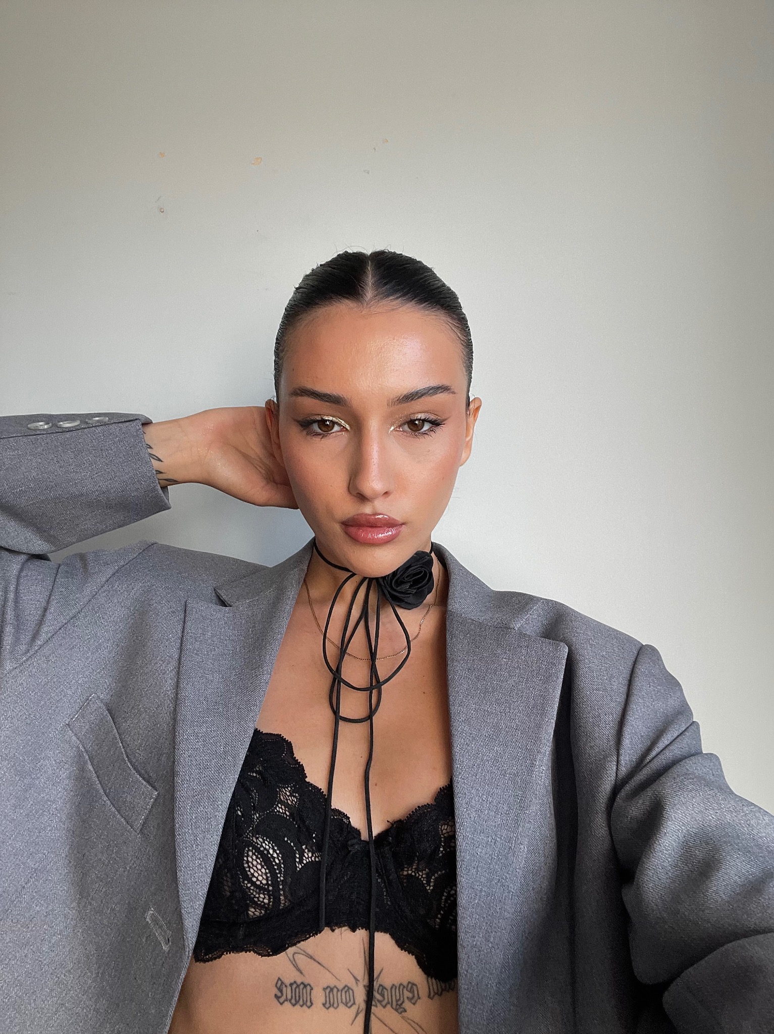 Portret kobiety w szarym żakiecie i koronkowej bieliźnie, z delikatnym makijażem i chokerem z czarną różą, na jasnym tle. Ujęcie centralne, podkreślające urodę modelki.