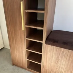 Drewniana szafa z półkami i siedziskiem w Kielcach, wykończona fornirem o ciepłym odcieniu. Widoczny złoty uchwyt i minimalistyczny design.