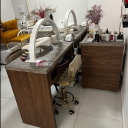 Richmont meble - Długi, drewniany stół do manicure z marmurowym blatem, oświetleniem LED w kształcie łuku i krzesłami na złotych kółkach. Widoczne akcesoria do manicure i dekoracje.