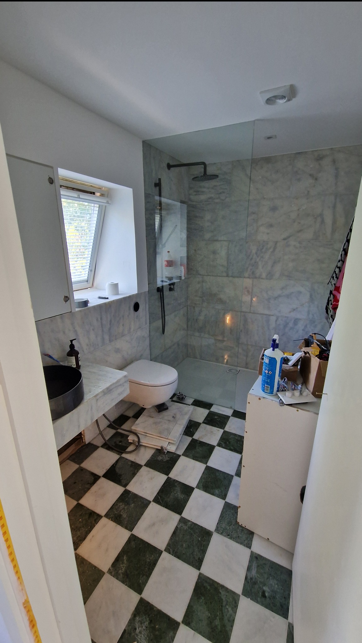 Remontowana łazienka z marmurowymi płytkami, czarną armaturą i wzorzystą podłogą. Widoczne narzędzia i materiały budowlane, co sugeruje etap wykończeniowy.