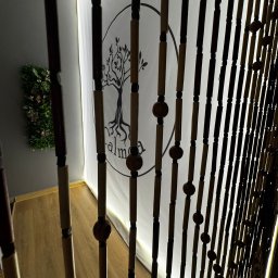 DIXIT SPÓŁKA Z OGRANICZONĄ ODPOWIEDZIALNOŚCIĄ - Wnętrze z drewnianą kurtyną, logo drzewa na ścianie i roślinną dekoracją. Ujęcie z dołu, podkreślające detale i głębię przestrzeni gabinetu.