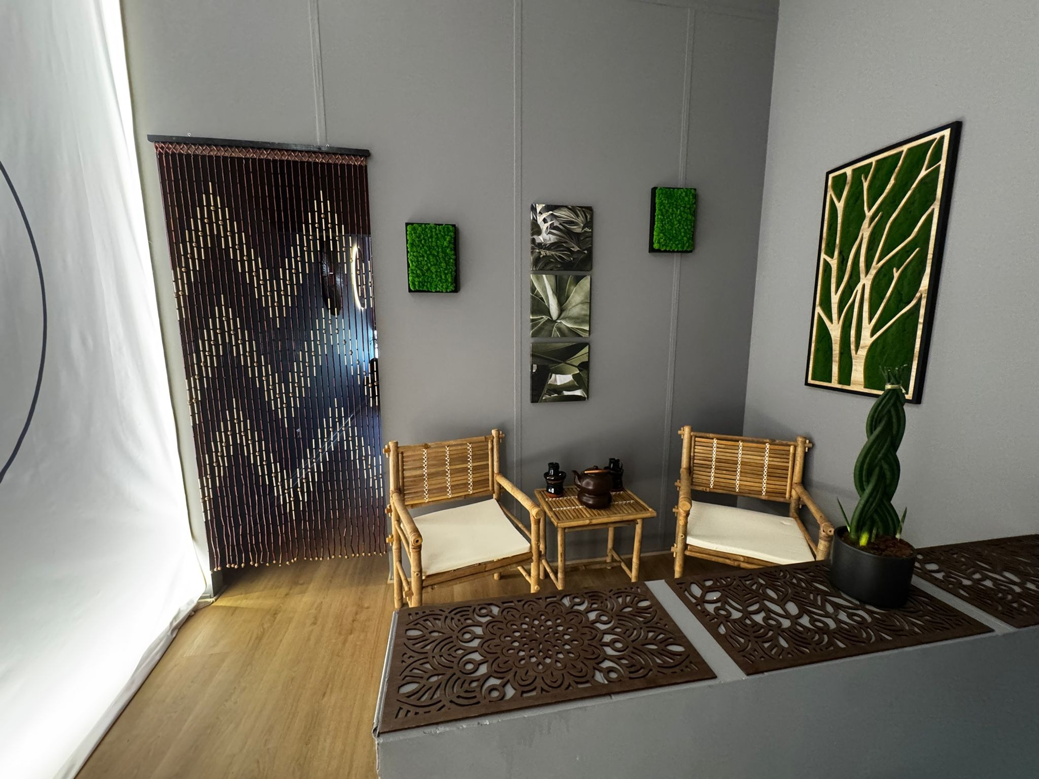 Stylowe wnętrze salonu masażu z bambusowymi krzesłami, stolikiem i dekoracjami roślinnymi na ścianach. Przytulna aranżacja, idealna do relaksu i odprężenia.