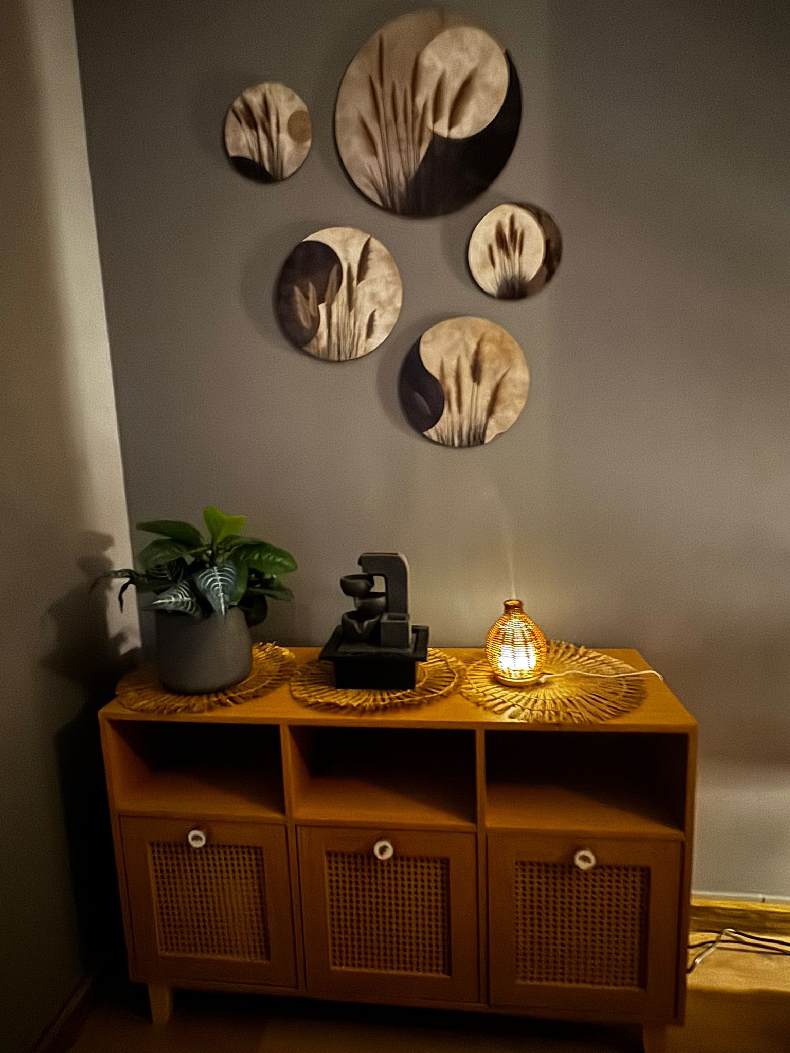 Stylowe wnętrze salonu kosmetycznego: drewniana komoda z dekoracjami, lampka zapachowa i rośliny. Okrągłe ozdoby na ścianie tworzą relaksującą atmosferę.