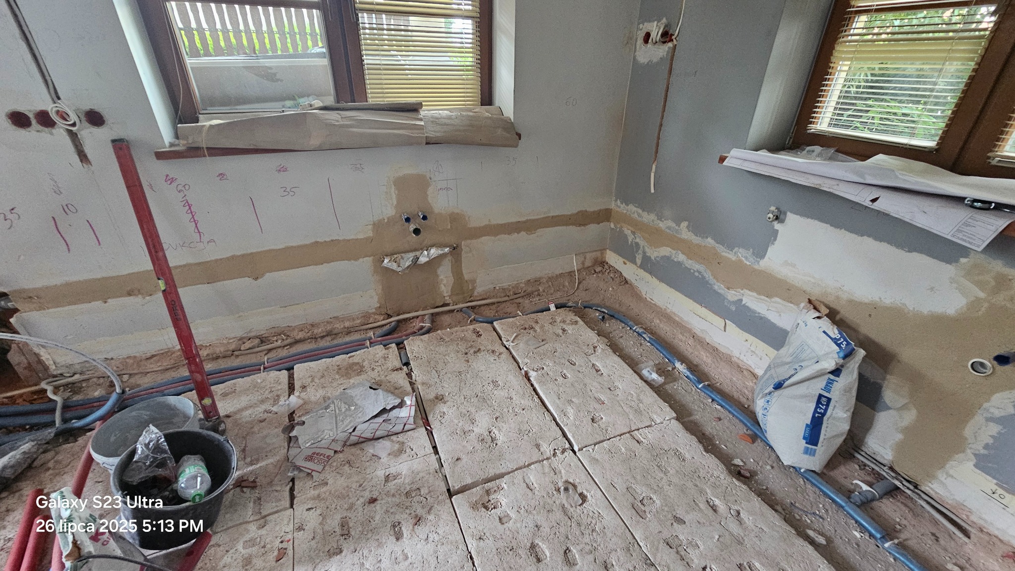 Montaż ogrzewania podłogowego: widok na ułożone płyty izolacyjne z rurami instalacji grzewczej w trakcie prac wykończeniowych w pomieszczeniu z oknem i instalacją.