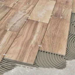 Układanie płytek imitujących drewno na podłodze, widoczny klej i krzyżyki dystansowe. Ujęcie z góry, jasne oświetlenie.