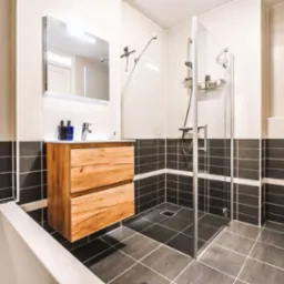 Nowoczesna łazienka z kabiną prysznicową, drewnianą szafką pod umywalką i czarno-białymi płytkami. Grzejnik drabinkowy z ręcznikiem.