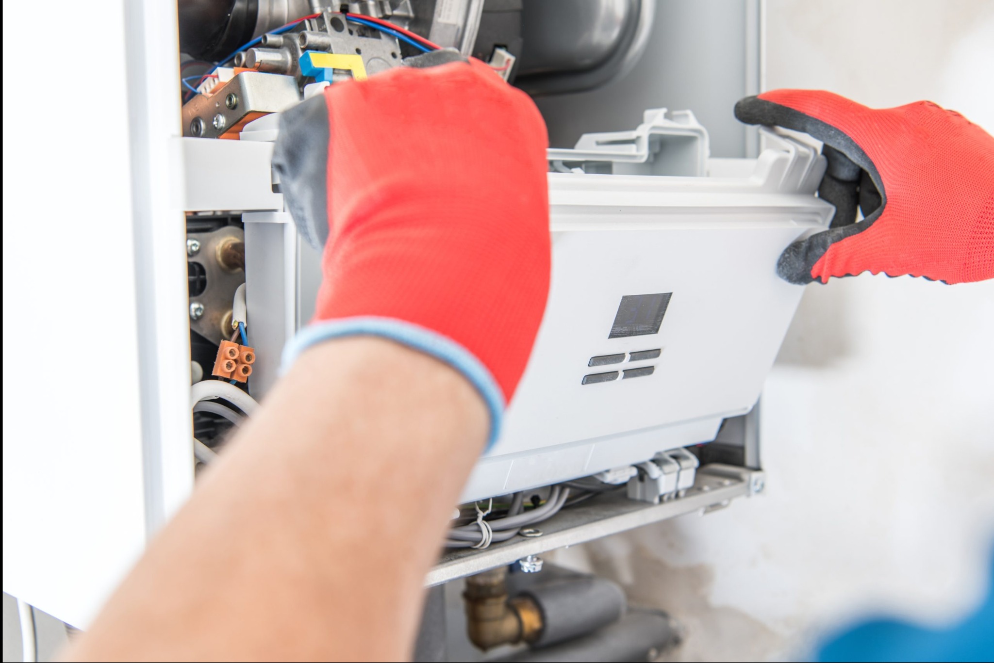 Otwarty piec gazowy, serwisowany przez technika w czerwonych rękawicach. Widoczne przewody i elementy wewnętrzne urządzenia, biała obudowa w trakcie demontażu.