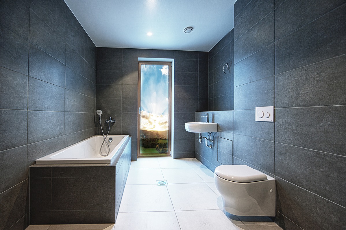 Nowoczesna łazienka z szarymi płytkami, białą armaturą i widokiem na krajobraz przez okno. Minimalistyczny design z wanną, umywalką i toaletą.