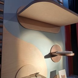 .bygga - USŁUGI MICHAŁ BIGUS - Błękitno-drewniana konstrukcja z półkami o zaokrąglonych kształtach, w stylu minimalistycznym. Na jednej z półek leży kartka z ceną. Widoczne elementy drabinki.