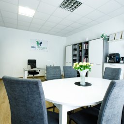 DDL PROGRES - Gabinet psychologiczny Zabrze - Jasne wnętrze biura z okrągłym stołem, szarymi krzesłami, kwiatami, regałem, certyfikatami i logo firmy DDL PROGRES na ścianie. Nowoczesny i profesjonalny wystrój.