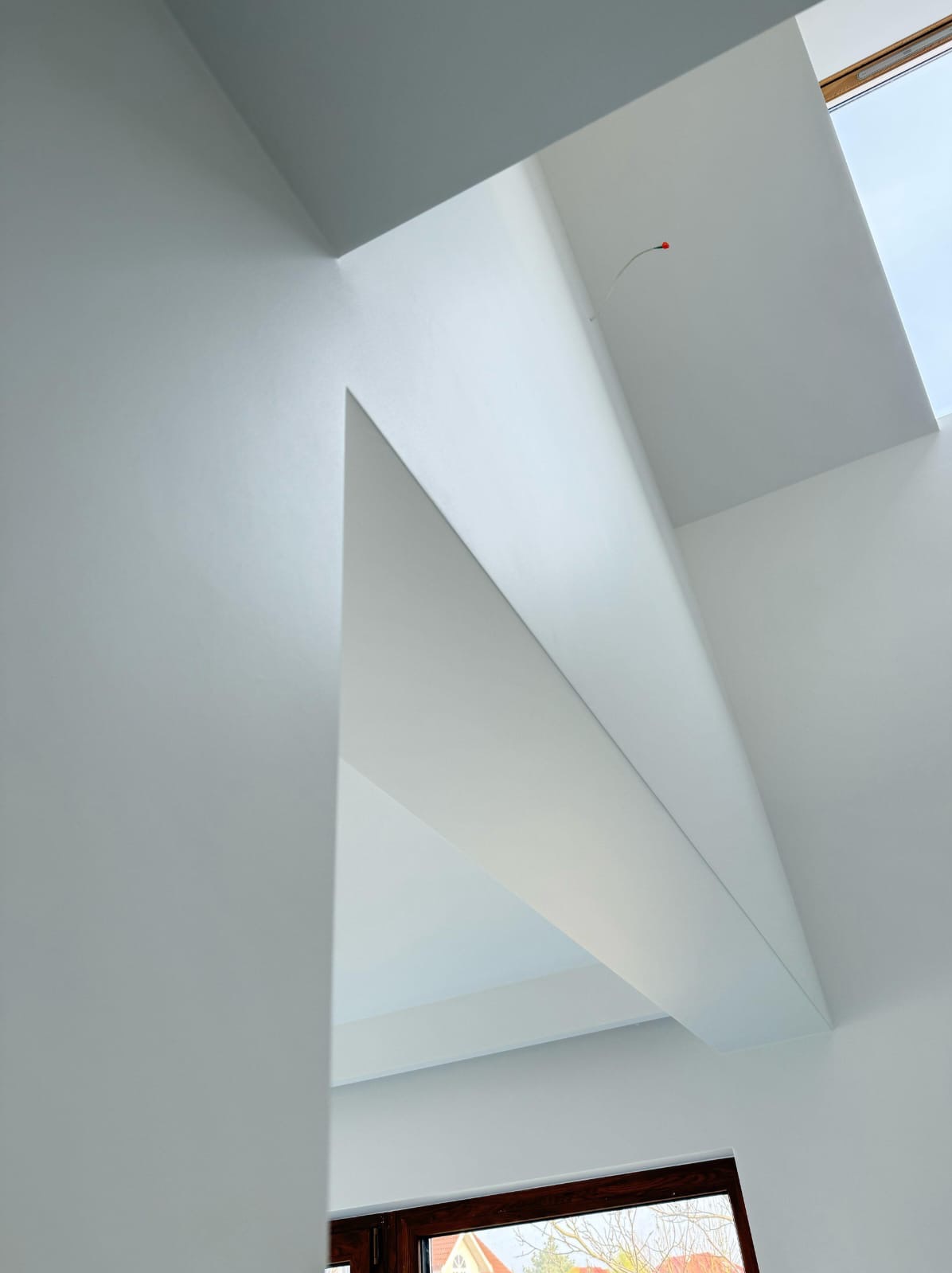 Białe, gładkie ściany i sufit w nowoczesnym wnętrzu z oknem dachowym. Widok z dołu, podkreślający geometrię i minimalizm wykończenia.