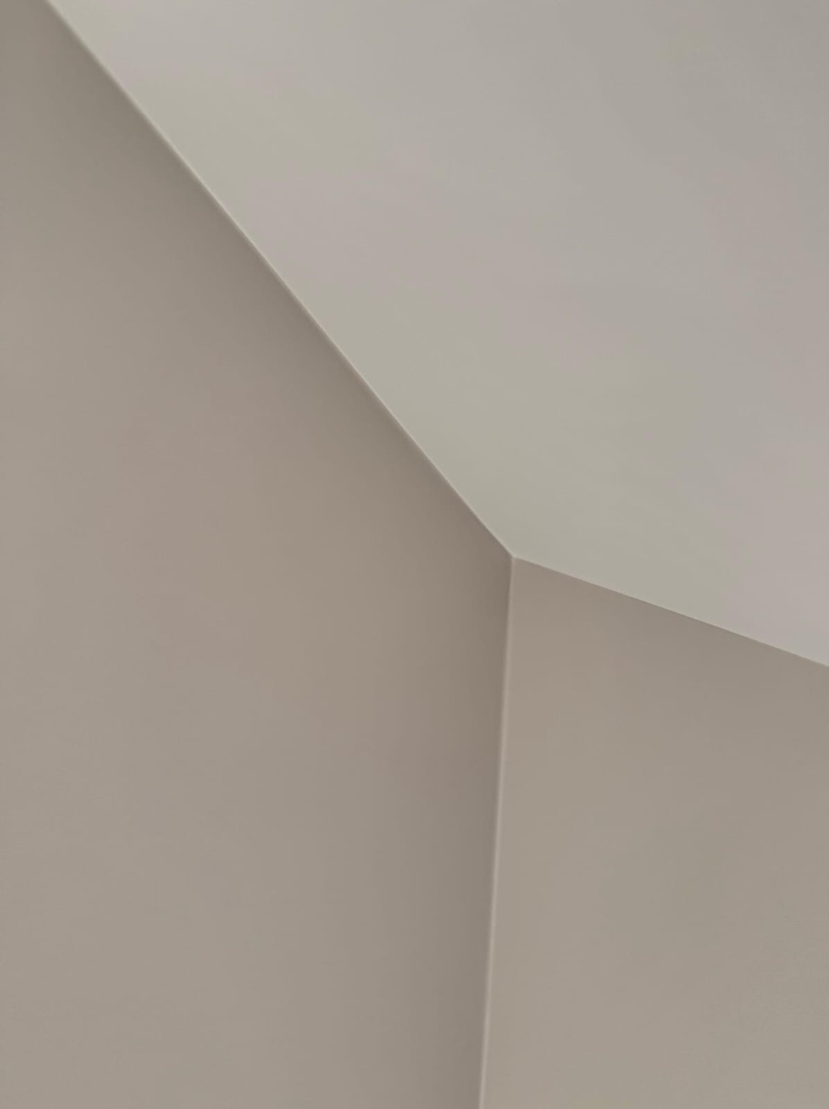 Pomieszczenie po malowaniu: gładkie ściany w odcieniach beżu i bieli, widoczne połączenie ściany z sufitem pod kątem, minimalistyczny kadr.