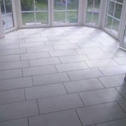 Radosław No - Białe, prostokątne płytki podłogowe w jasnym pomieszczeniu z dużymi oknami wychodzącymi na zieleń. Minimalistyczny design i świeże wykończenie.