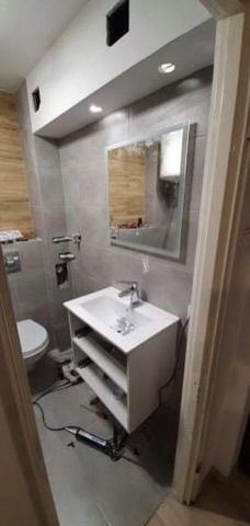 Wykończona łazienka z szarymi płytkami, białą szafką pod umywalką i lustrem. Widoczne narzędzia sugerują etap końcowy prac.