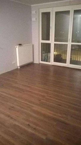 Ukończona podłoga z paneli w pokoju z grzejnikiem i dużymi oknami balkonowymi. Widok na parkiet z bliska.