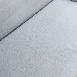 V.P.M.M. Profiti - Jasnoszara, czysta kanapa z bliska. Widoczna faktura materiału i delikatne światło. Minimalistyczny design mebla.