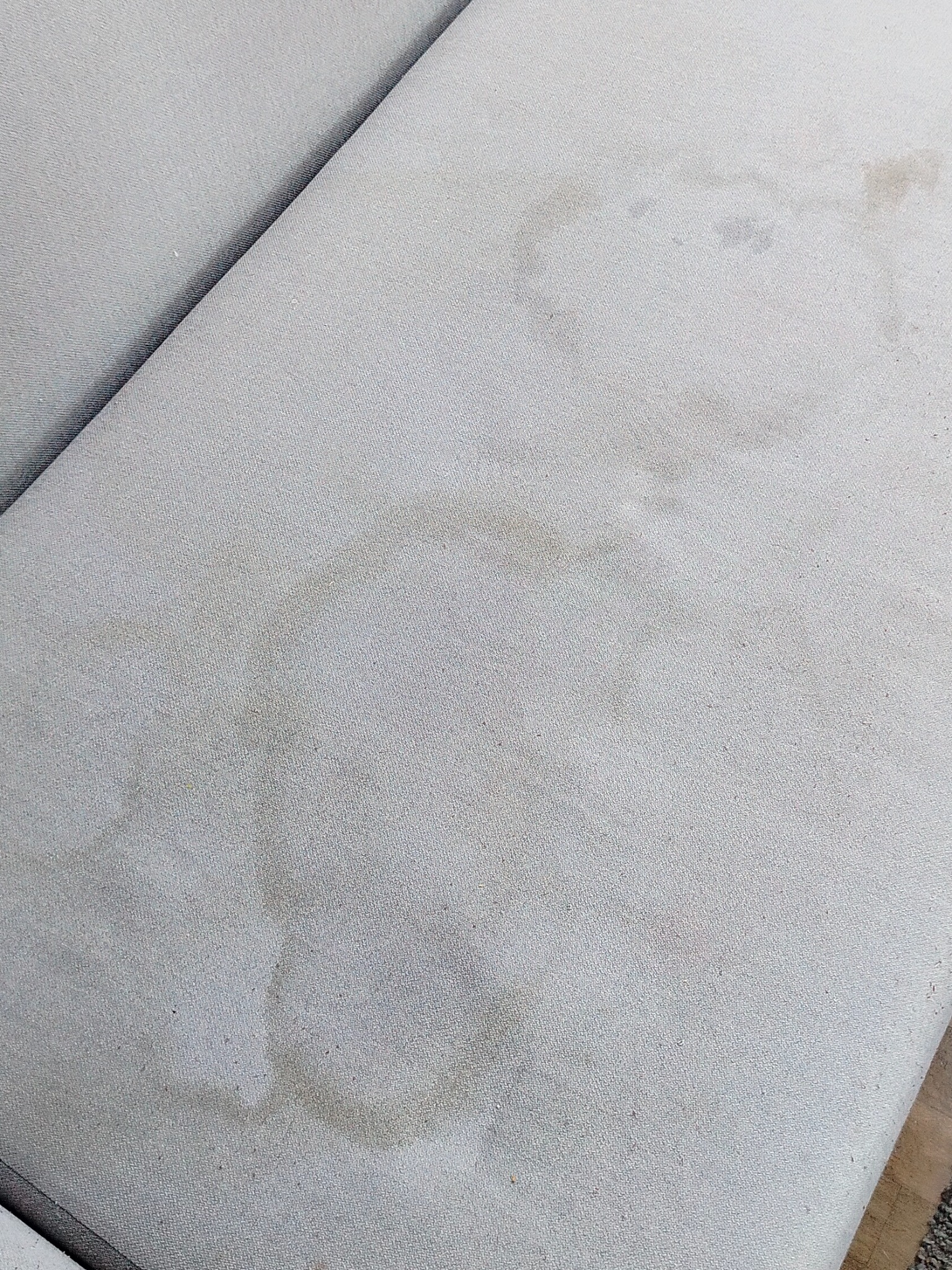 Jasnoszara tapicerka sofy z widocznymi, okrągłymi plamami. Widok z góry, ukazujący zabrudzenia na siedzisku. Tekstura materiału dobrze widoczna.