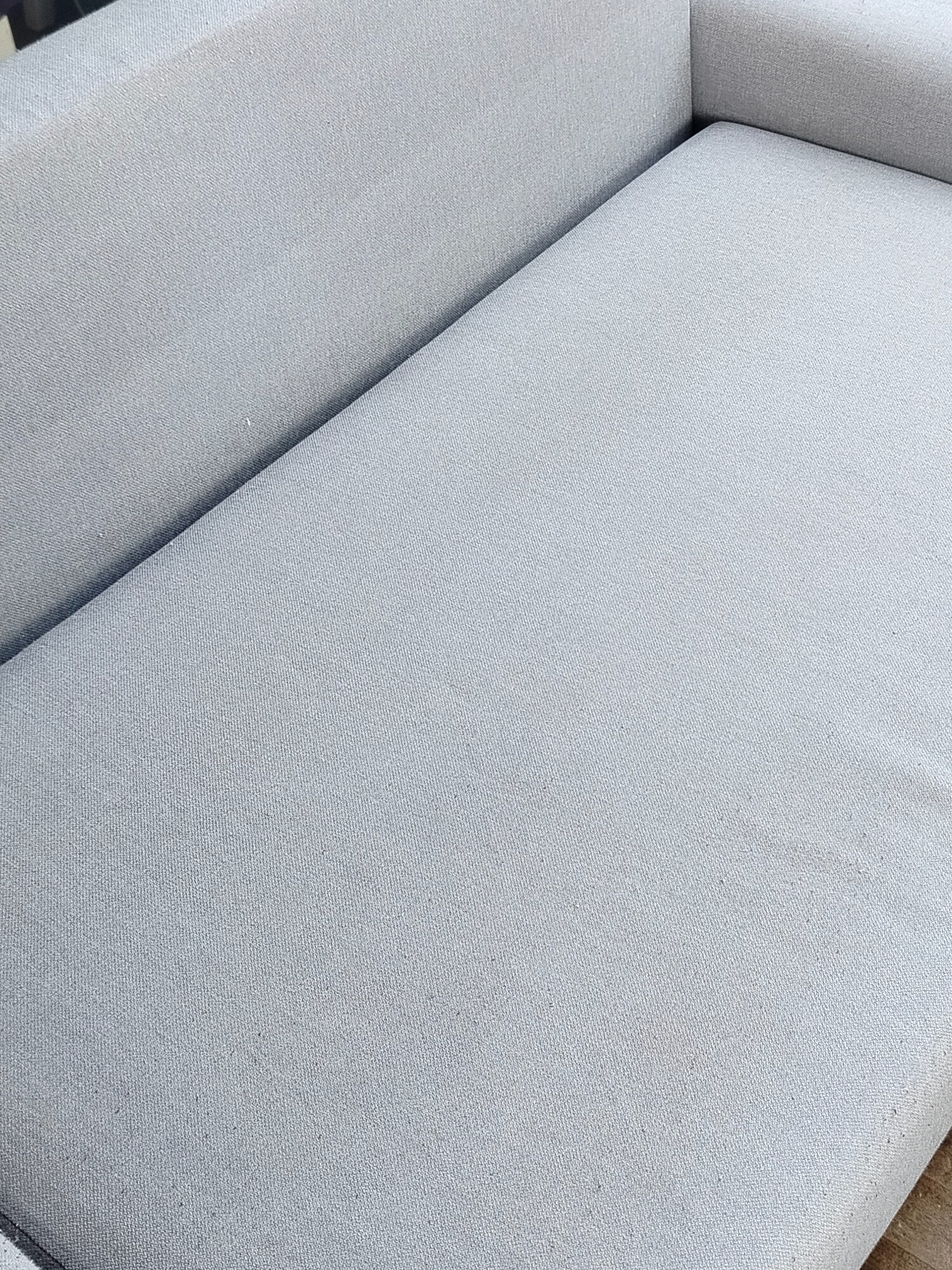 Jasnoszara, czysta kanapa z bliska. Widoczna faktura materiału i delikatne światło. Minimalistyczny design mebla.