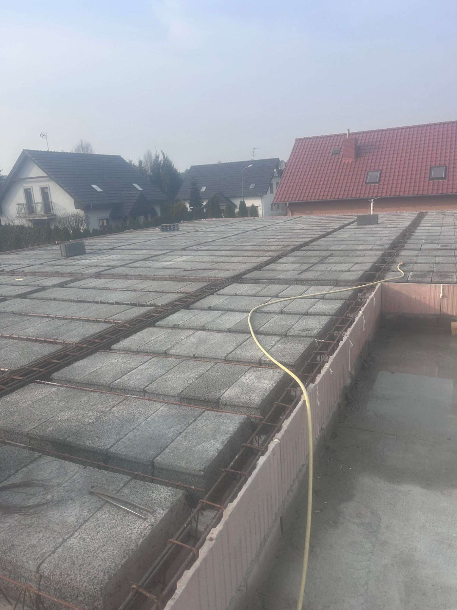 Zbrojenie stropu Teriva z betonowych pustaków, widoczne pręty i piankowe szalunki. W tle domy jednorodzinne. Ujęcie z góry, lekka mgła.