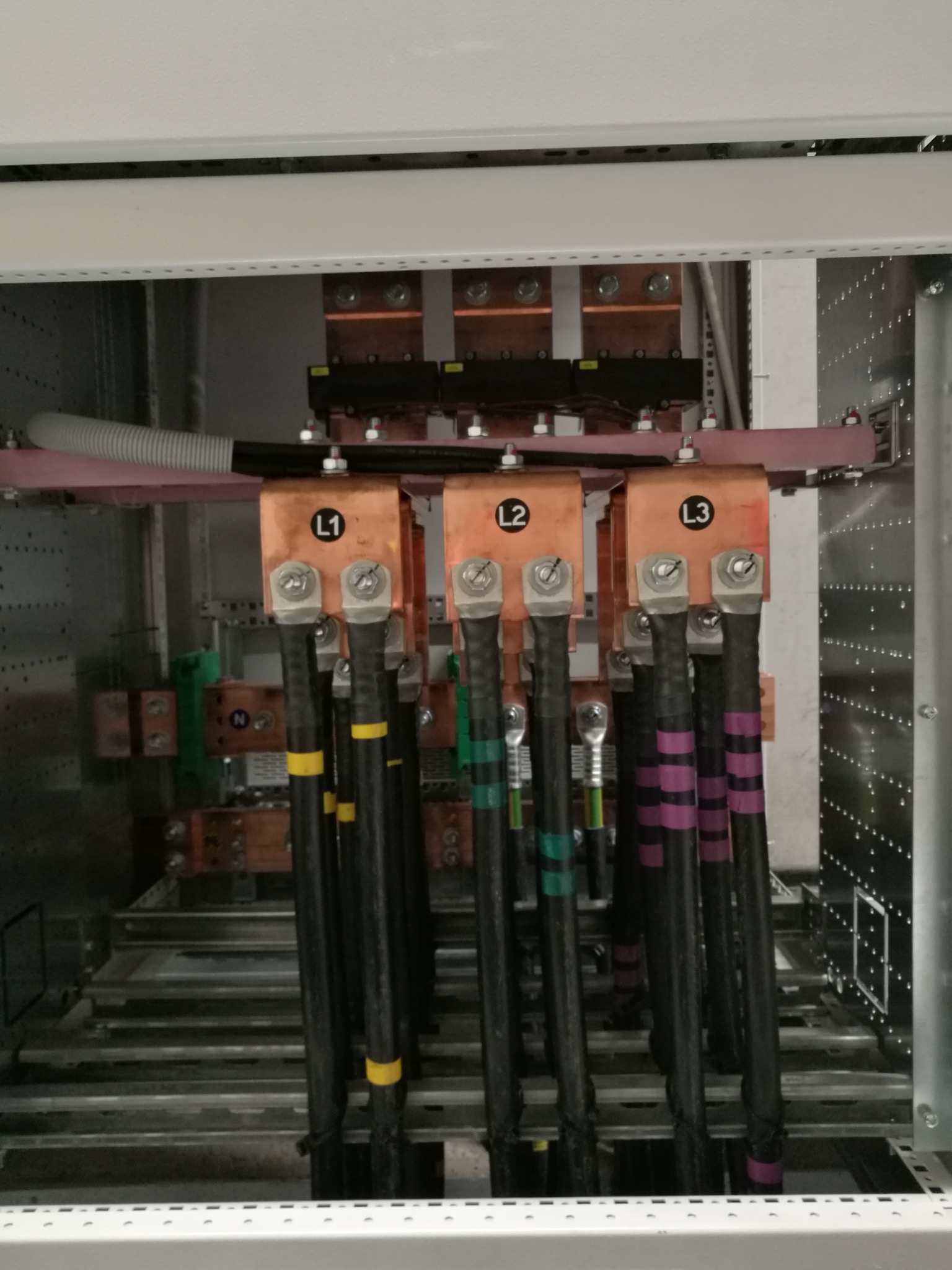 Szczegółowe ujęcie instalacji elektrycznej w rozdzielnicy, z widocznymi przewodami oznaczonymi L1, L2, L3 oraz kolorowymi paskami identyfikacyjnymi.