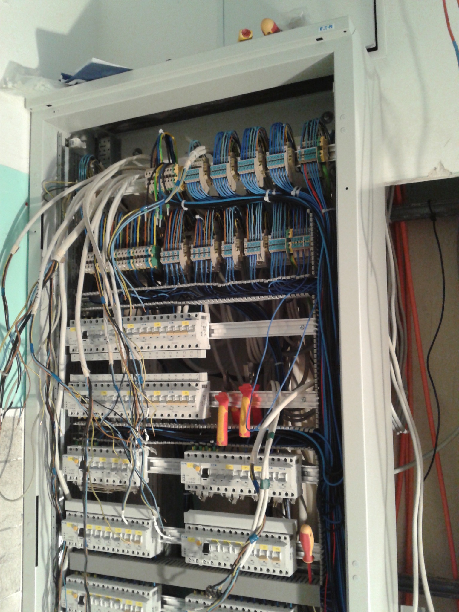 Rozdzielnica elektryczna z licznymi kablami i bezpiecznikami, widoczne narzędzia. Uporządkowane okablowanie wewnątrz szafy sterowniczej, detale połączeń.