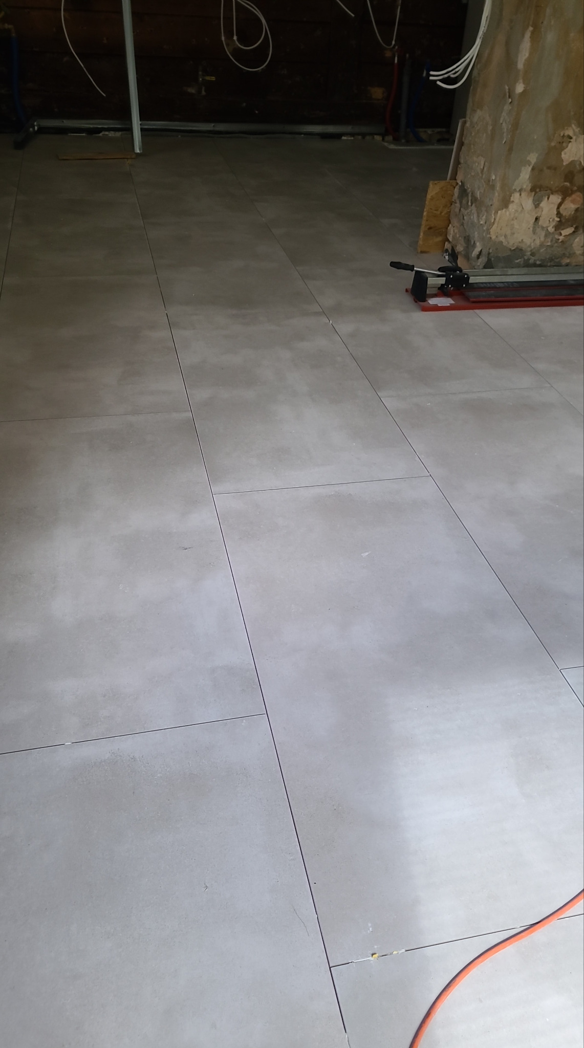 Ułożone, szare płytki podłogowe w trakcie remontu. Widoczny fragment ściany w stanie surowym i narzędzie glazurnicze.