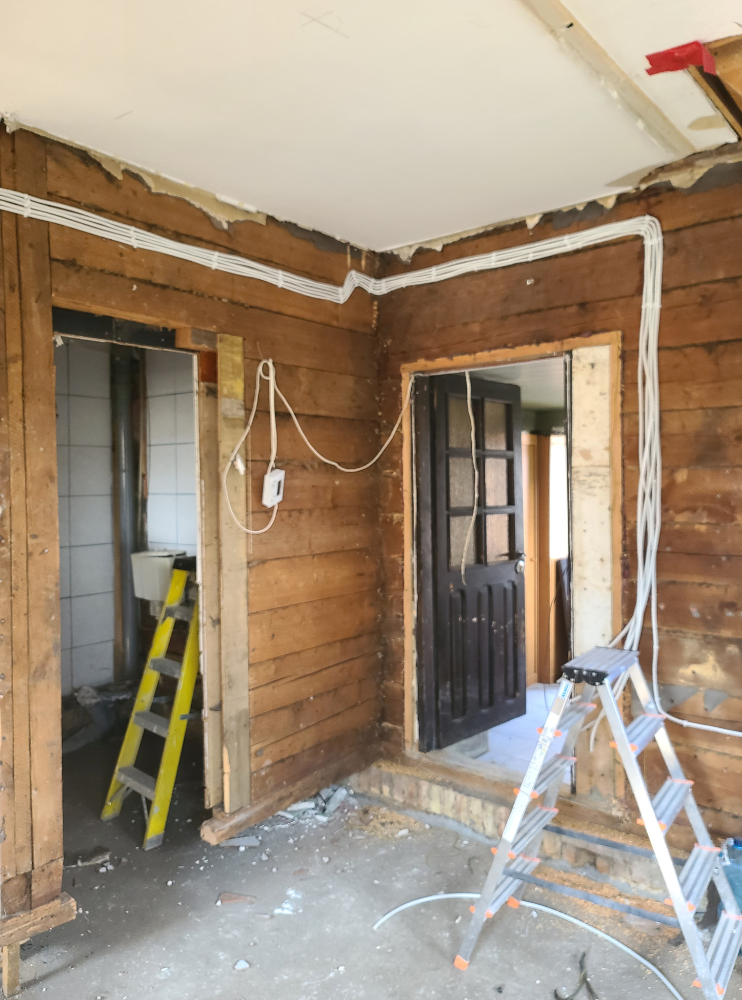 Instalacja elektryczna w drewnianym domu w trakcie remontu. Widoczne kable, ściany z desek, drabiny i gruz. Prace przygotowawcze do wykończenia wnętrza.