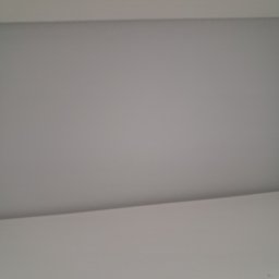 CONTRAST GRZEGORZ BORKOWSKI - Gładka, pomalowana na szaro powierzchnia sufitu z widocznym fragmentem białej listwy przysufitowej. Minimalistyczne wykończenie wnętrza.