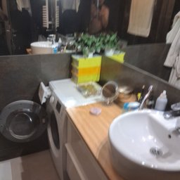 CONTRAST GRZEGORZ BORKOWSKI - Nowoczesna łazienka z umywalką nablatową, pralką i dużym lustrem, w którym odbija się osoba. Ciemne płytki i drewniany blat dodają elegancji.