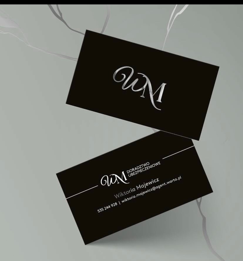 Dwie czarne wizytówki z srebrnym logo 'WM' i danymi kontaktowymi Wiktorii Majewicz, doradcy ubezpieczeniowego, na tle marmurowej powierzchni.