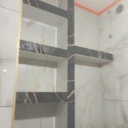 Półki wnękowe z płytek imitujących marmur, czarne obramowanie, pomarańczowe akcenty w wykończonej łazience. Nowoczesny design.