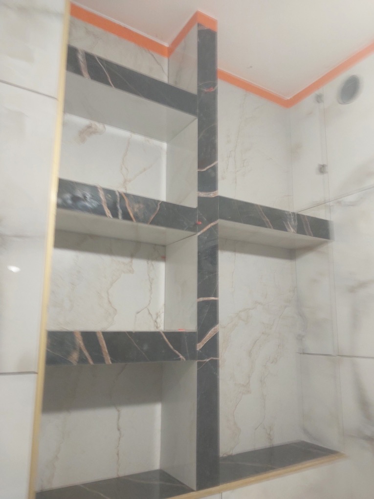 Półki wnękowe z płytek imitujących marmur, czarne obramowanie, pomarańczowe akcenty w wykończonej łazience. Nowoczesny design.