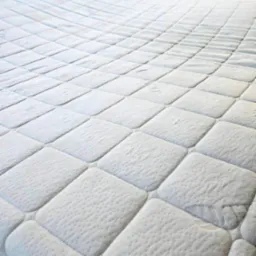 Wypełniony, biały materac z pikowaniem w romby, ukazujący czystą powierzchnię po praniu. Widoczne delikatne wzory i tekstura materiału.