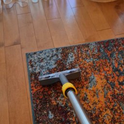 KRAKÓW TOP CLEAN IGOR GOGUNSKYI - Czyszczenie wzorzystego dywanu na podłodze z desek za pomocą odkurzacza piorącego z żółtymi elementami. Widoczne zasłony i lampa w tle.