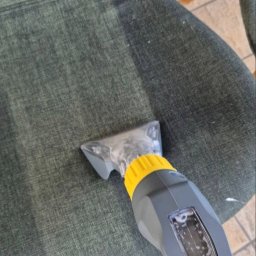 KRAKÓW TOP CLEAN IGOR GOGUNSKYI - Czyszczenie tapicerki krzesła tekstylnego przy użyciu odkurzacza piorącego. Widoczna różnica w kolorze po praniu. Płytki podłogowe w tle. Ujęcie z góry.