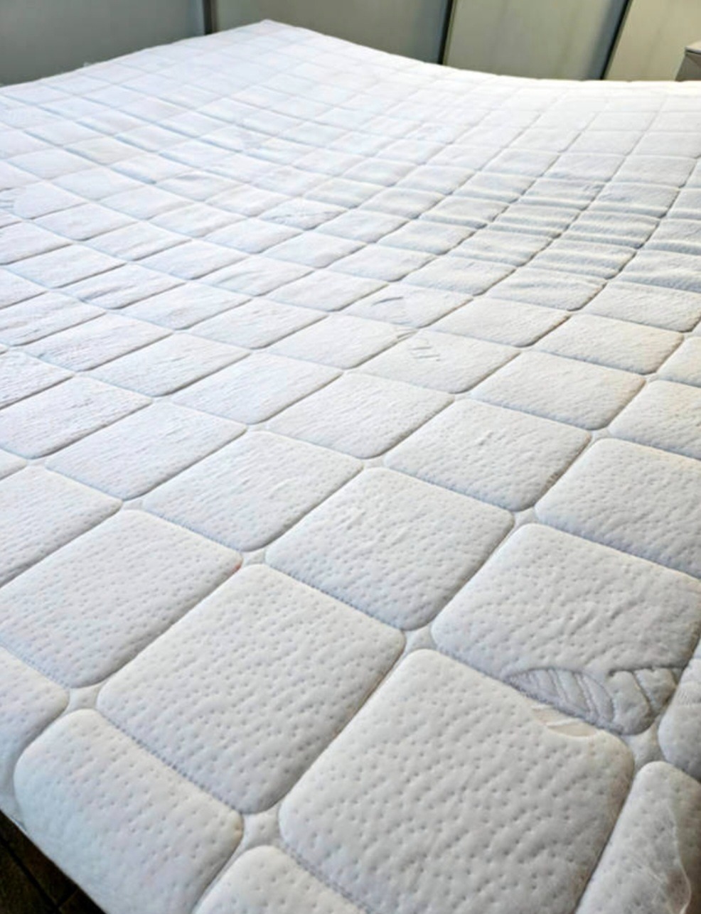 Wypełniony, biały materac z pikowaniem w romby, ukazujący czystą powierzchnię po praniu. Widoczne delikatne wzory i tekstura materiału.