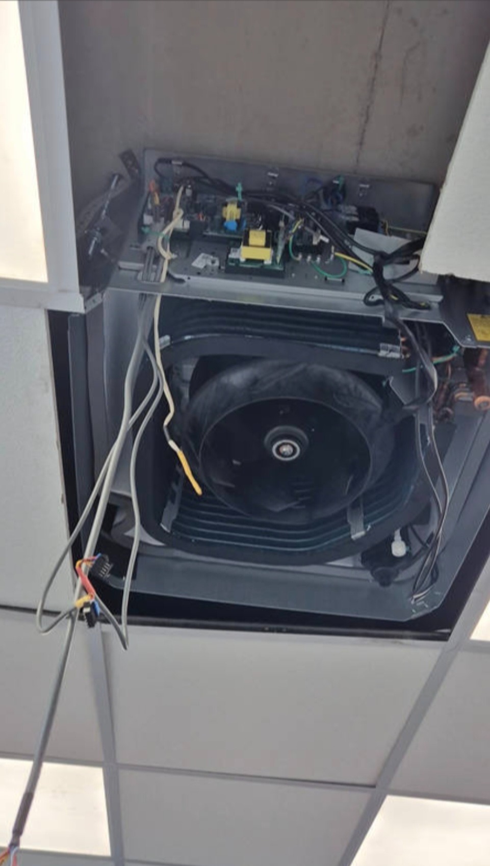 Otwarta obudowa klimatyzacji kasetonowej w suficie podwieszanym, widoczne elementy wewnętrzne: wentylator, elektronika i przewody. Przegląd techniczny klimatyzacji.