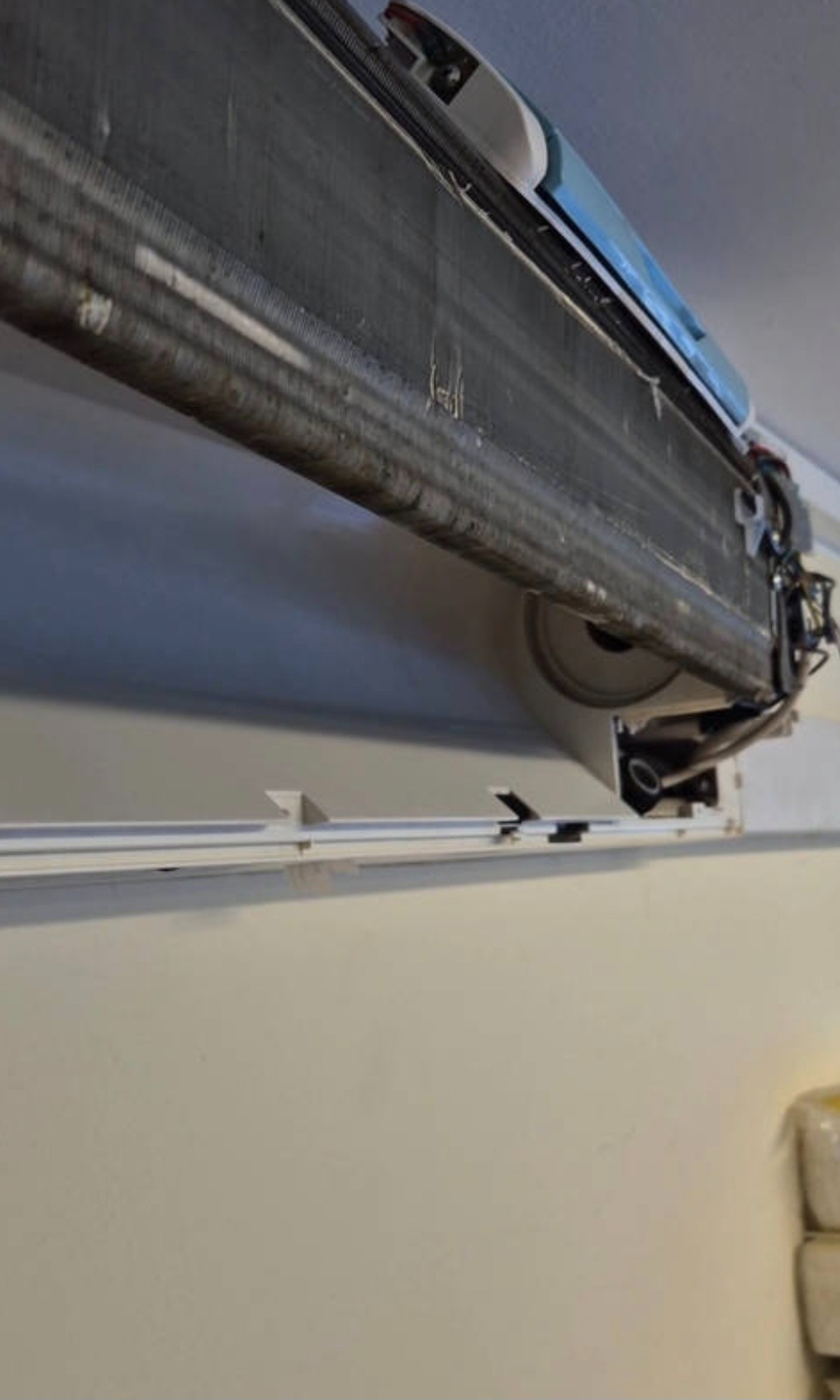 Widok z dołu na otwarty klimatyzator ścienny, ukazujący żebra chłodzące i elementy wewnętrzne. Widoczne przewody i filtry. Ściana w tle jest jasna.