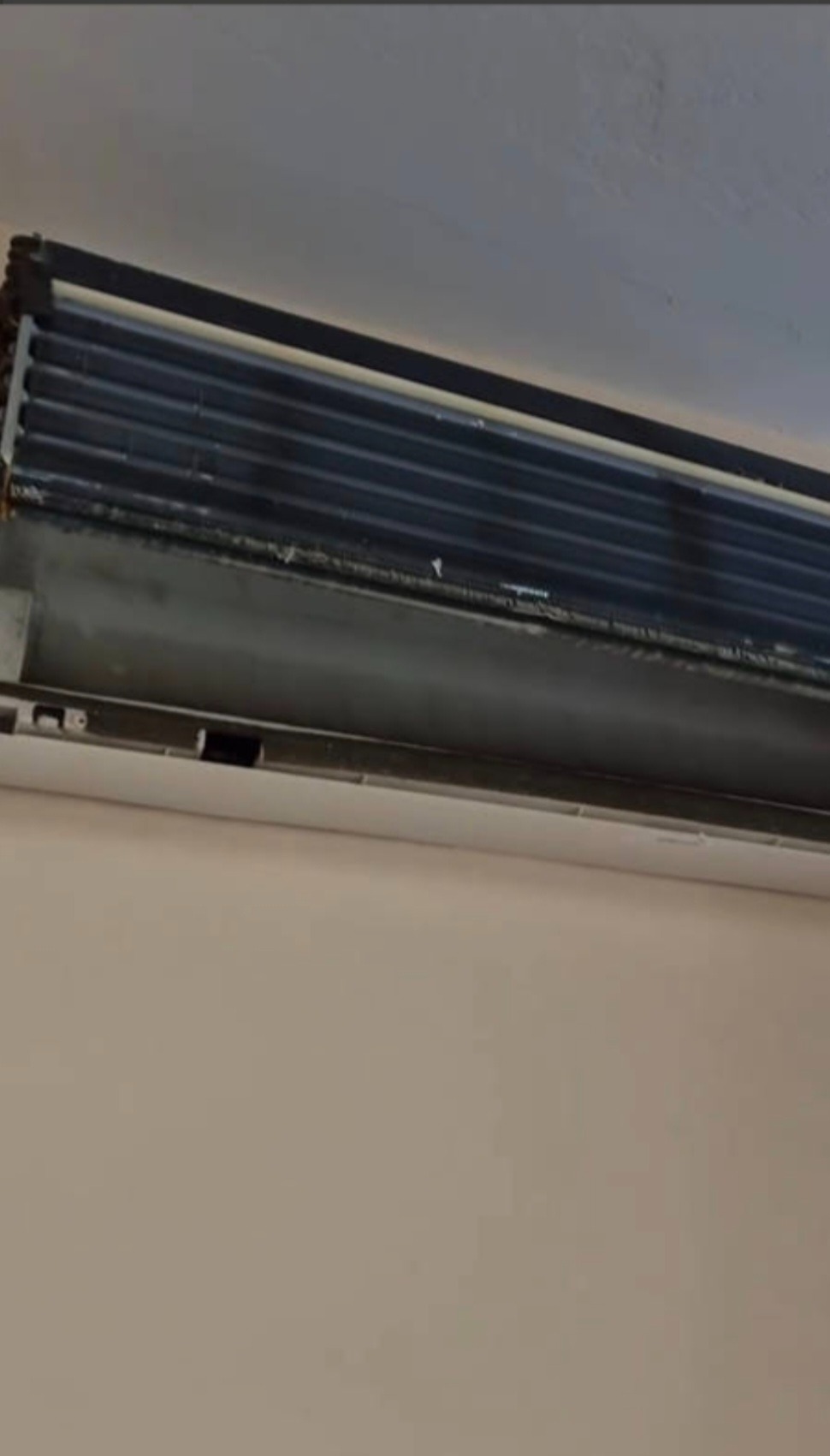 Otwarty, brudny klimatyzator ścienny, widoczne żebra chłodzące. Urządzenie w kolorze białym, zamontowane na jasnej ścianie.